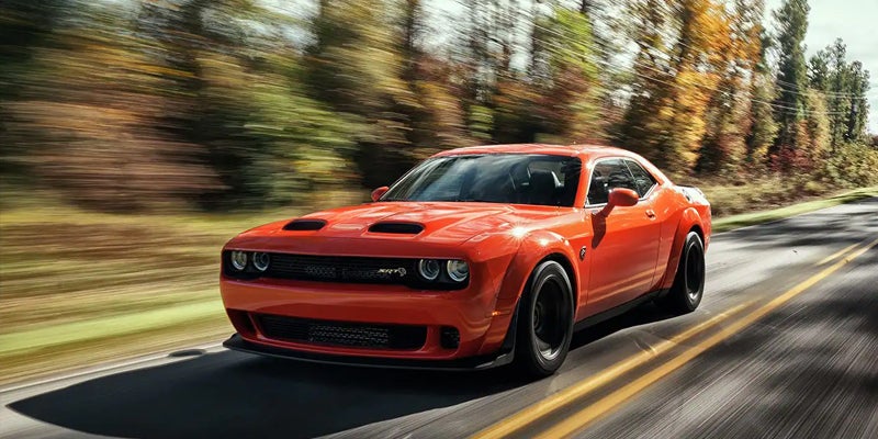 Orange Dodge Challenger SRT driving on a forest road.